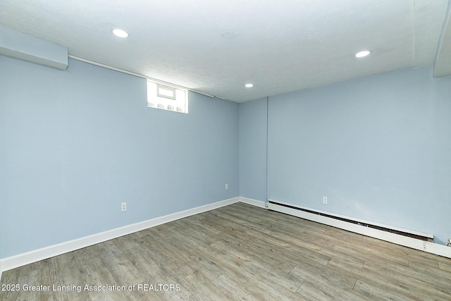 below grade area featuring light wood finished floors, baseboards, a baseboard heating unit, and recessed lighting