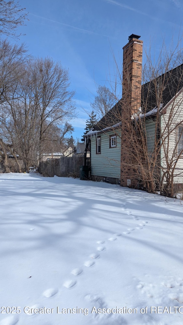 view of snow covered exterior with a chimney and fence