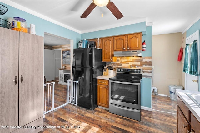 kitchen with under cabinet range hood, electric stove, light countertops, freestanding refrigerator, and brown cabinetry