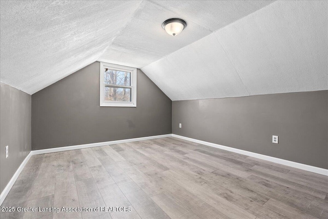 additional living space with light wood finished floors, baseboards, vaulted ceiling, and a textured ceiling