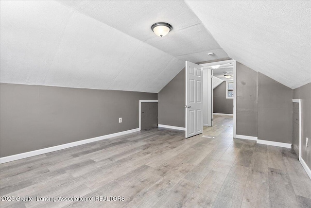 additional living space with lofted ceiling, a textured ceiling, light wood-type flooring, and baseboards