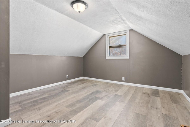 additional living space with a textured ceiling, vaulted ceiling, light wood-style flooring, and baseboards