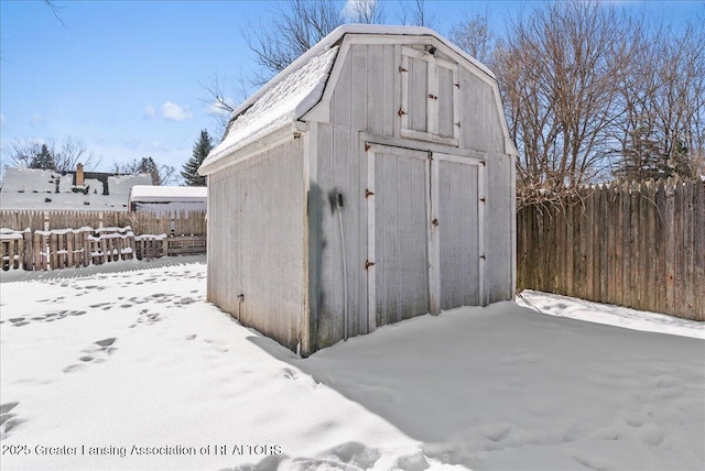 snow covered structure featuring fence, an outdoor structure, and a shed