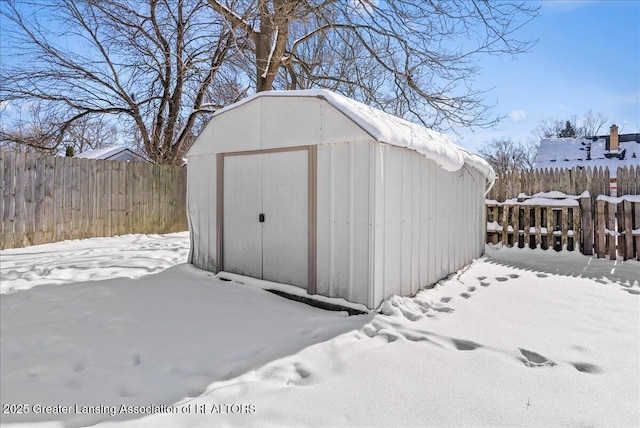 snow covered structure with a shed, an outdoor structure, and fence