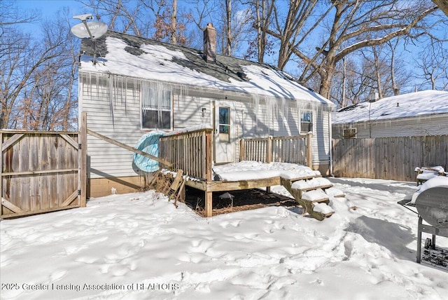 snow covered house featuring a gate, a chimney, fence, and a wooden deck