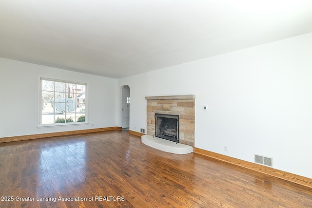 unfurnished living room with visible vents, baseboards, a stone fireplace, wood finished floors, and arched walkways