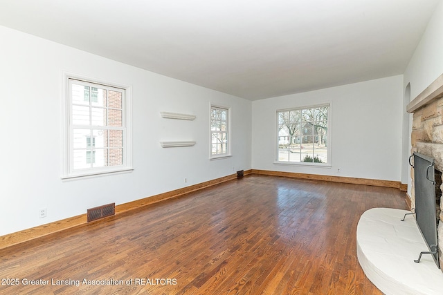 unfurnished living room featuring dark wood-style flooring, a fireplace, visible vents, and a wealth of natural light