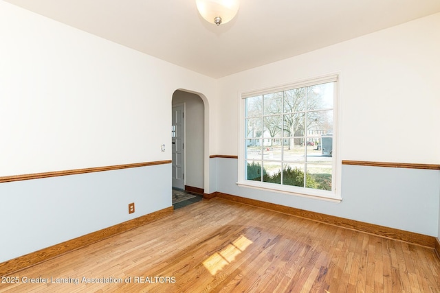 unfurnished room featuring light wood-style flooring, baseboards, and arched walkways