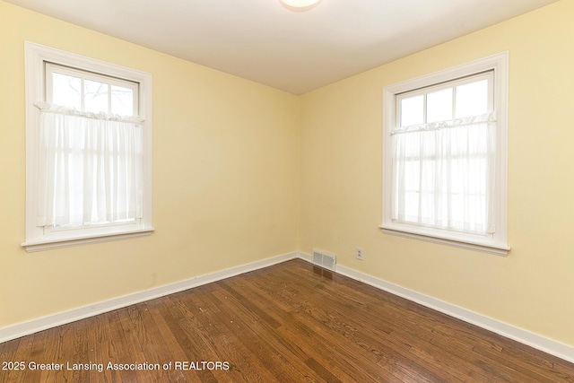 spare room with visible vents, baseboards, and dark wood-style flooring