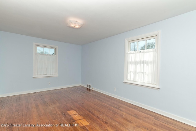 unfurnished room featuring visible vents, dark wood-style floors, a healthy amount of sunlight, and baseboards