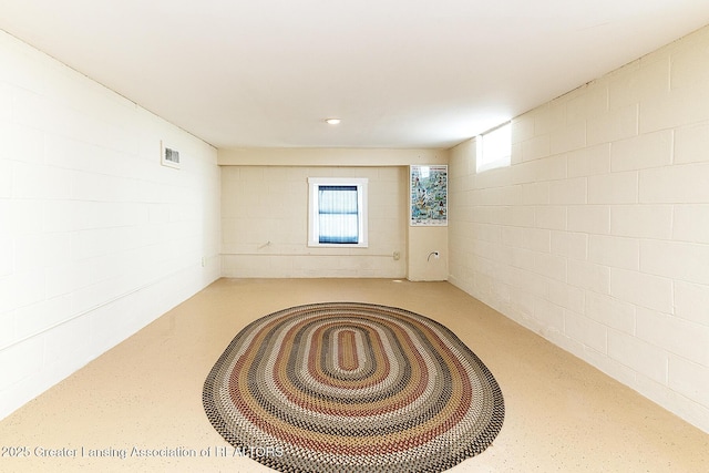 empty room with concrete block wall, finished concrete flooring, visible vents, and plenty of natural light