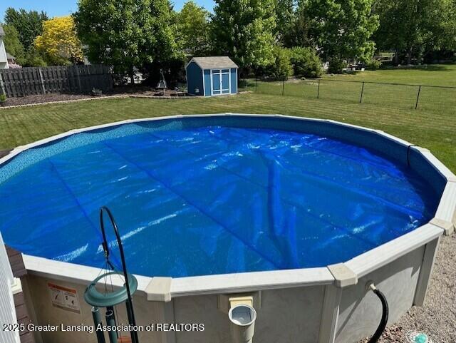 view of swimming pool featuring a yard, a fenced backyard, an outdoor structure, and a storage shed