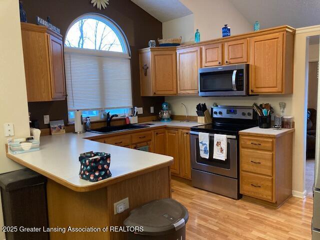 kitchen featuring stainless steel appliances, light countertops, a sink, and a peninsula