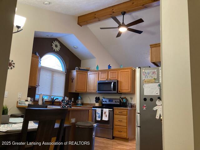 kitchen with light wood finished floors, lofted ceiling with beams, appliances with stainless steel finishes, brown cabinetry, and a ceiling fan