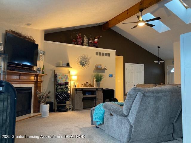 carpeted living area with vaulted ceiling with skylight, visible vents, a fireplace with raised hearth, and ceiling fan