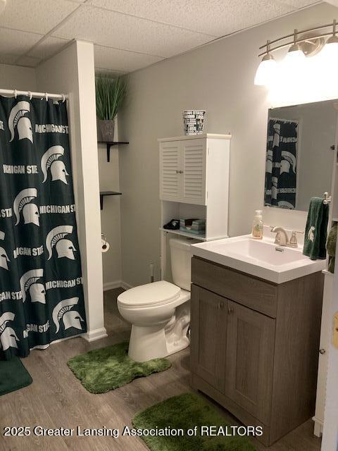 full bath with curtained shower, toilet, vanity, wood finished floors, and a drop ceiling