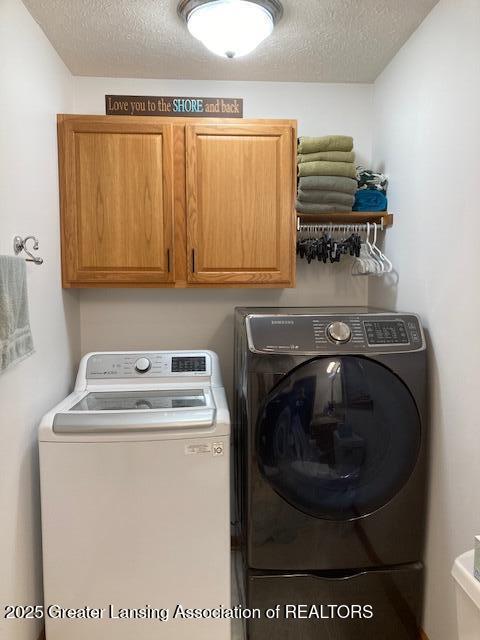 washroom with cabinet space, washer and clothes dryer, and a textured ceiling