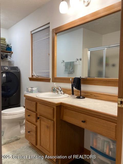 bathroom featuring toilet, vanity, a shower stall, tile patterned floors, and washer / dryer