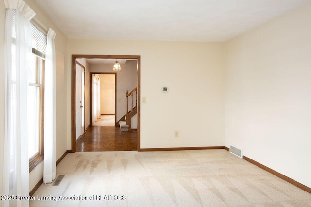 carpeted spare room featuring stairs, visible vents, and baseboards