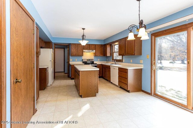 kitchen with white appliances, a kitchen island, brown cabinets, light countertops, and a sink