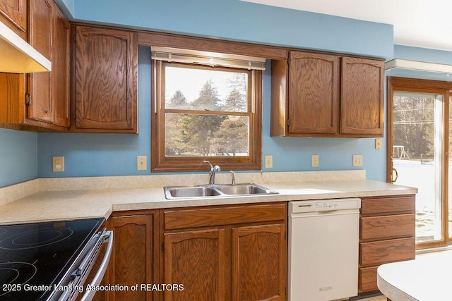 kitchen featuring dishwasher, brown cabinets, light countertops, under cabinet range hood, and a sink