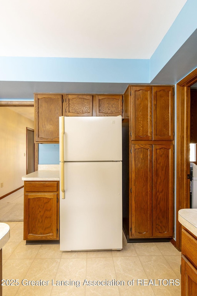 kitchen featuring light tile patterned floors, light countertops, brown cabinetry, freestanding refrigerator, and baseboards