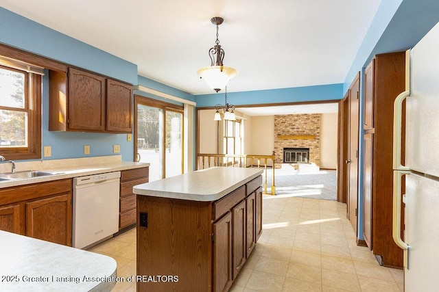 kitchen featuring white appliances, light countertops, a brick fireplace, a center island, and pendant lighting