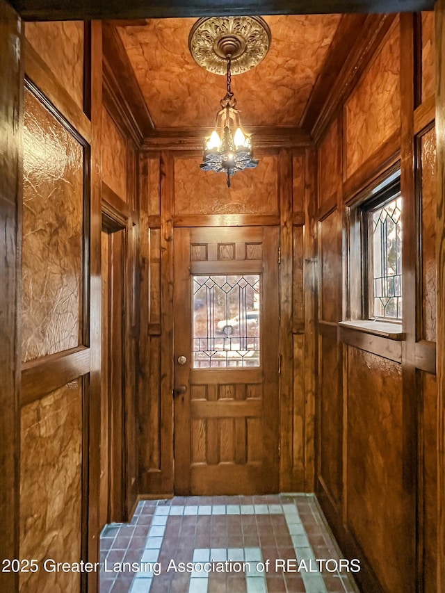 entryway with wood walls, a chandelier, and ornamental molding