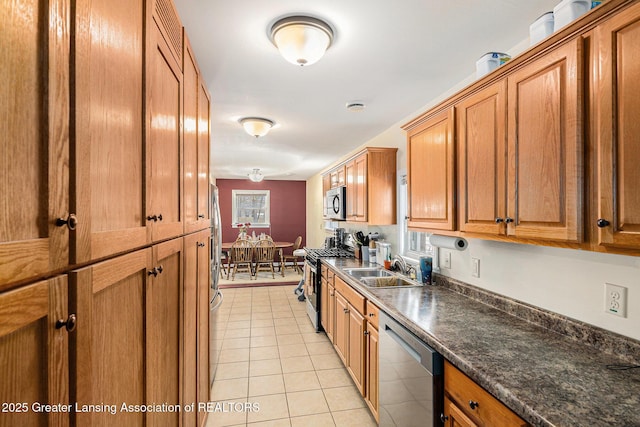 kitchen featuring dark stone counters, brown cabinetry, appliances with stainless steel finishes, a sink, and light tile patterned flooring