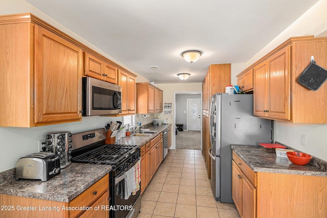 kitchen featuring brown cabinets, light tile patterned floors, stainless steel appliances, and a sink