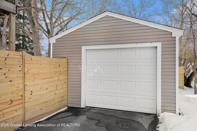 snow covered garage with a detached garage and fence