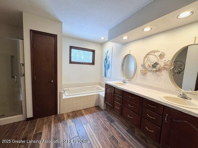 bathroom with a garden tub, a textured ceiling, a sink, and wood finished floors