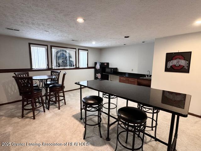 dining area featuring indoor wet bar, visible vents, light carpet, a textured ceiling, and baseboards