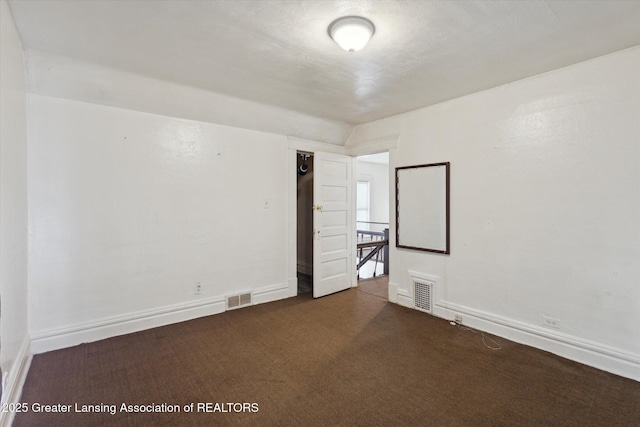 spare room with baseboards, visible vents, and dark carpet