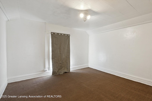 unfurnished room with lofted ceiling, baseboards, and dark carpet