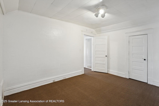 empty room with dark colored carpet, lofted ceiling, and baseboards