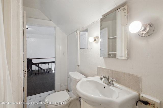 half bathroom with lofted ceiling, a sink, and toilet