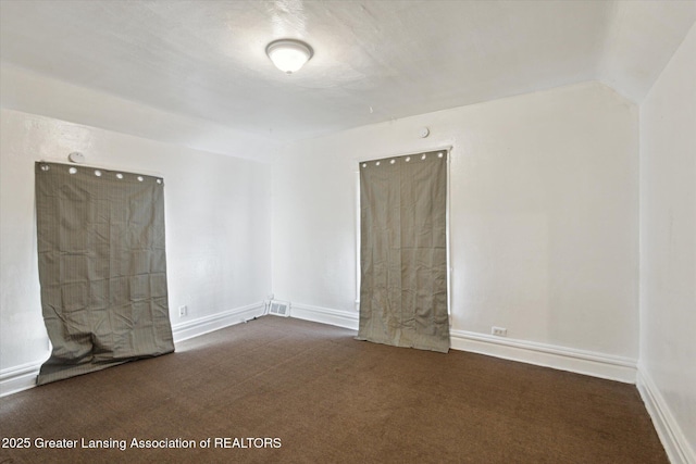 empty room with vaulted ceiling, baseboards, and dark colored carpet