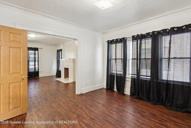 spare room featuring ornamental molding, a brick fireplace, dark wood finished floors, and baseboards