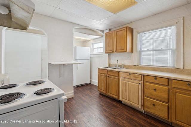 kitchen featuring a paneled ceiling, white appliances, a sink, light countertops, and dark wood-style floors