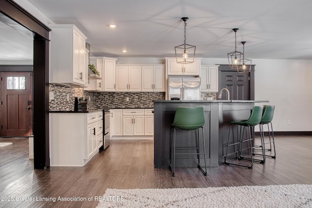 kitchen with a kitchen island with sink, appliances with stainless steel finishes, decorative backsplash, dark countertops, and decorative light fixtures