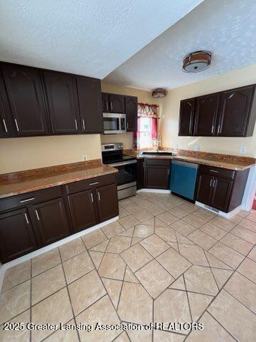 kitchen featuring a textured ceiling, stainless steel appliances, dark brown cabinets, and light tile patterned floors