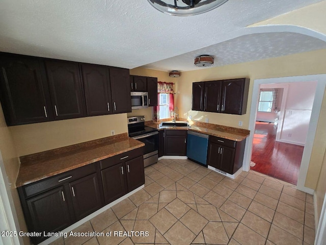 kitchen with dark countertops, a textured ceiling, appliances with stainless steel finishes, and a sink