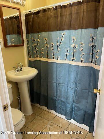 bathroom with toilet, curtained shower, a sink, and tile patterned floors