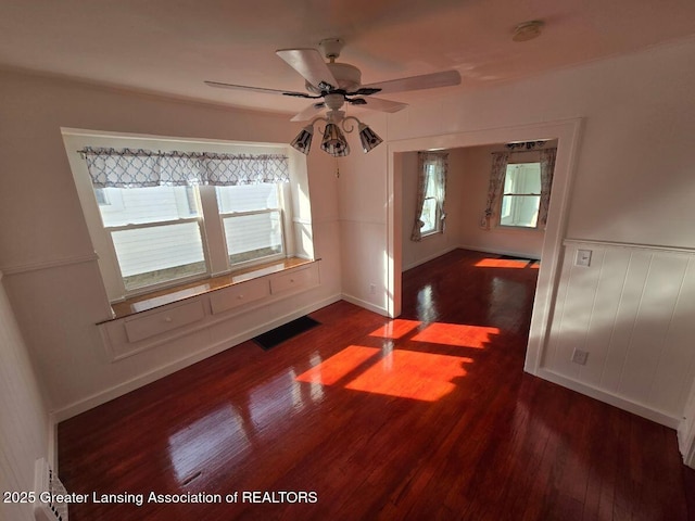 empty room featuring ceiling fan, visible vents, dark wood finished floors, and wainscoting