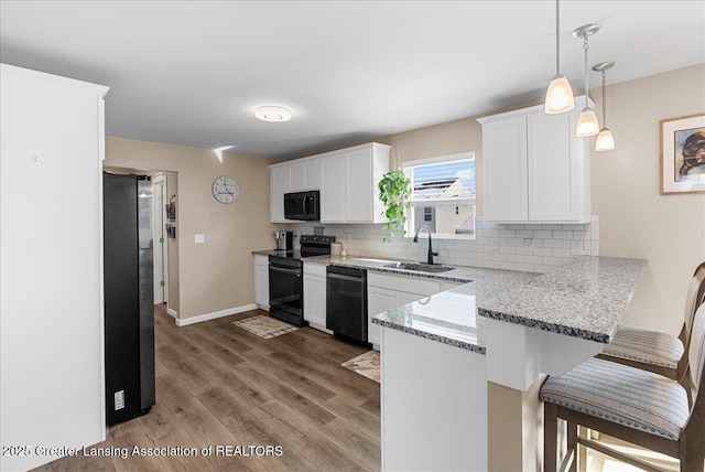 kitchen with a peninsula, a sink, black appliances, a kitchen bar, and backsplash