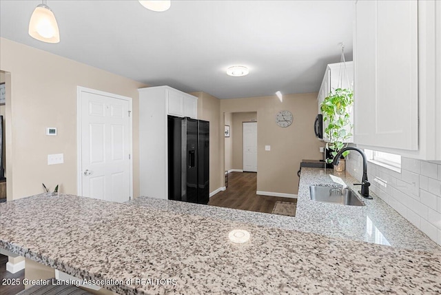 kitchen featuring light stone counters, a sink, white cabinetry, decorative backsplash, and black refrigerator with ice dispenser