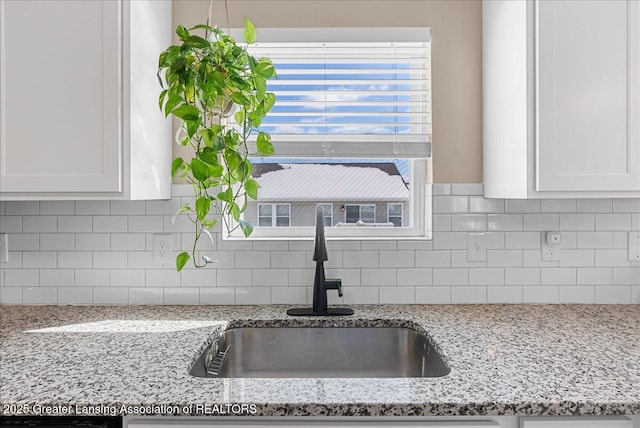 kitchen with white cabinets, light stone countertops, backsplash, and a sink