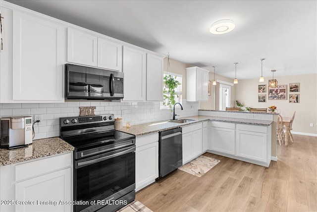 kitchen featuring white cabinets, a peninsula, stainless steel appliances, light wood-type flooring, and a sink