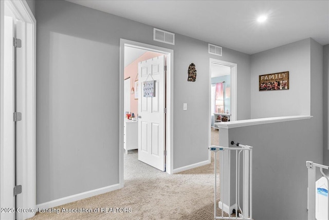 hallway featuring carpet, visible vents, baseboards, and an upstairs landing